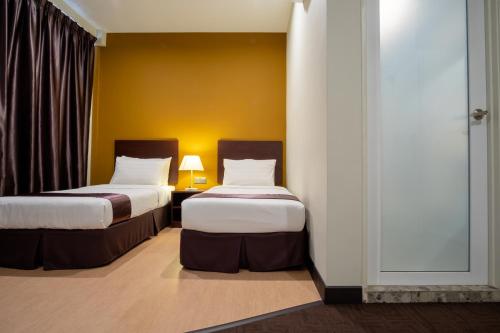 two beds in a hotel room with yellow walls at Orkid Inn Mahkota Cheras in Kampong Perimbun