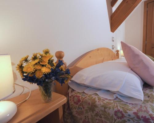a vase of flowers on a table next to a bed at Albergo Diffuso Ravascletto in Ravascletto