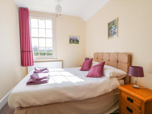 a bedroom with a bed with pink pillows and a window at South Lodge - Longford Hall Farm Holiday Cottages in Ashbourne