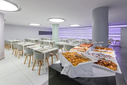 a cafeteria with white tables and white chairs and food on display at Hotel Garbi Ibiza & Spa in Playa d'en Bossa