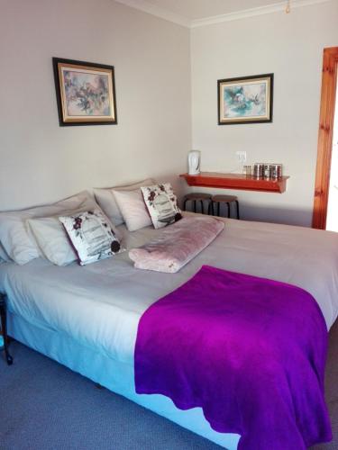a bedroom with a large bed with a purple blanket on it at The Olde House in Port Elizabeth