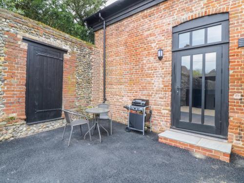 a patio with a table and chairs next to a brick building at Grange Barn in Hessett