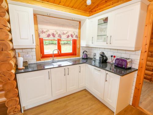 a kitchen with white cabinets and a sink and a window at Beech Lodge in Oakham