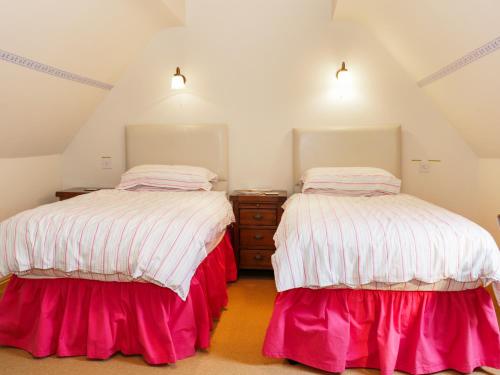 Duas camas num quarto no sótão com lençóis cor-de-rosa e brancos. em Wash House Cottage em Much Wenlock