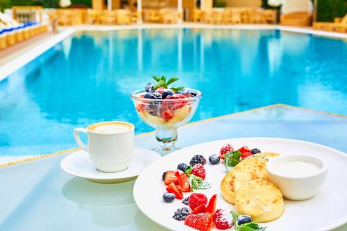 a breakfast of fruit and coffee next to a swimming pool at Palace Del Mar in Odesa