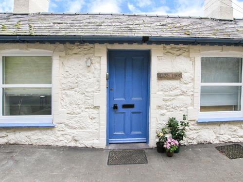 a stone cottage with a blue door and two windows at Glan Dwr Bach in Llandegfan