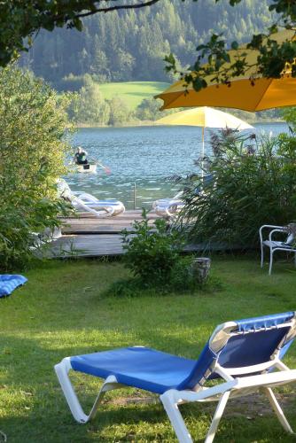 a blue and white chair sitting in the grass next to a lake at Landhaus Sonneck in Weissensee