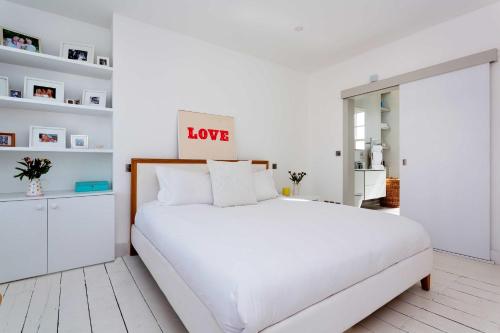 a white bedroom with a white bed and a love sign on the wall at Veeve - Princedale Road Minimalism in London