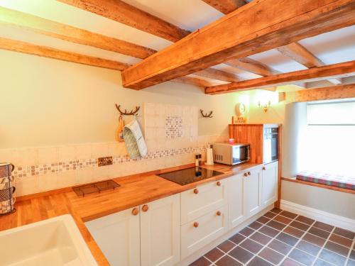 a kitchen with white cabinets and wooden ceilings at Jasmine Cottage in Belper
