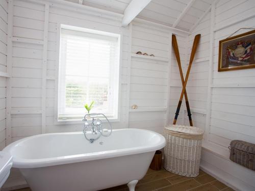 baño con bañera blanca y ventana en Lligwy Beach Cottage, en Penrhos-Lligwy
