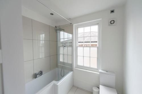 baño blanco con ducha y ventana en St Stephens Road Apartment, en Norwich