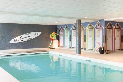 a man standing next to a swimming pool with a surfboard on a wall at ibis Styles Vierzon in Vierzon