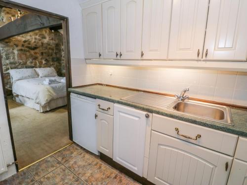 uma cozinha com armários brancos, um lavatório e uma cama em Waterfall Cottage em Caernarfon