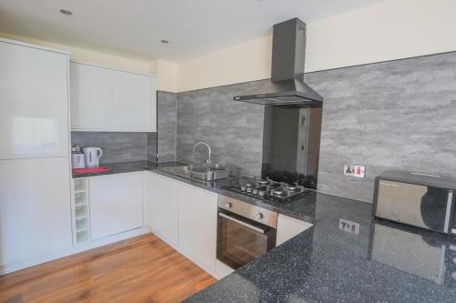 cocina con armarios blancos y encimera negra en Stylish Modern Newly Built Apartment 15 min From City Centre, en Edimburgo