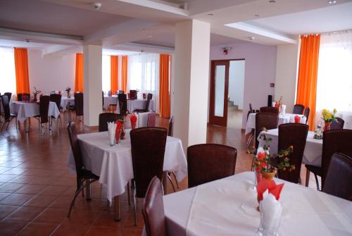 een eetkamer met witte tafels en stoelen en oranje gordijnen bij Pensiunea Bujor de Munte in Petroşani