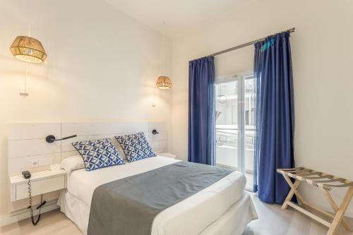 a bedroom with a bed with blue curtains and a window at FERGUS Style Soller Beach in Port de Soller