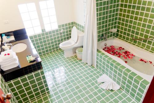 uma casa de banho com azulejos verdes, uma banheira e um WC. em Teak Garden Resort, Chiang Rai em Chiang Rai