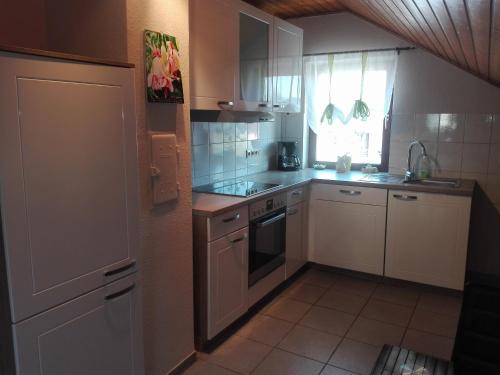 eine kleine Küche mit weißen Schränken und einem Fenster in der Unterkunft Obere Ferienwohnung Asshoff zwischen Odenwald, Taubertal und Bauland in Berolzheim