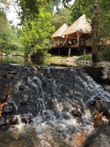 a hut next to a river with a waterfall at Rai Phusaitran ไร่ภูสายธาร in Mae Taeng