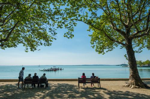 a group of people sitting on benches by the water at Füred Luxury Apartman with private pool in Balatonfüred