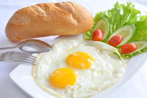 a white plate with eggs and bread and vegetables at Phong Nha Orient Hotel in Phong Nha