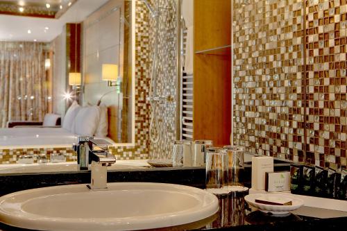 La salle de bains est pourvue d'un lavabo et d'un grand miroir. dans l'établissement Best Western PLUS Grim's Dyke Hotel, à Harrow