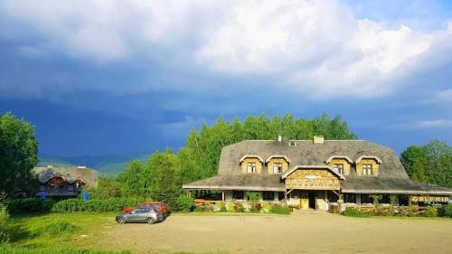 uma casa com telhado de palha e um carro estacionado em frente em Karczma Brzeziniak em Cisna