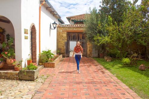 a woman walking down a brick walkway in front of a house at Posada Portal de la Villa in Villa de Leyva