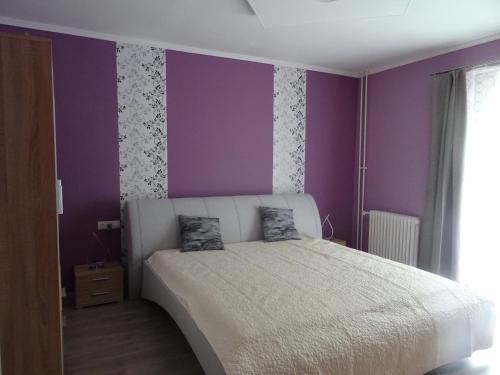 um quarto com paredes roxas e uma cama branca em Győri úti lakás em Tatabánya