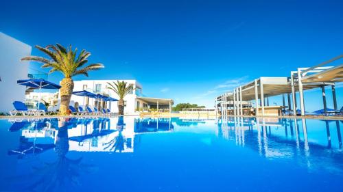a swimming pool with a palm tree and buildings at Adele Beach Hotel in Adelianos Kampos