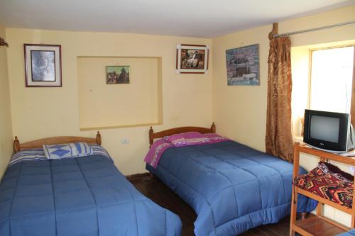 a bedroom with two beds and a tv and a window at Las Portadas in Ollantaytambo