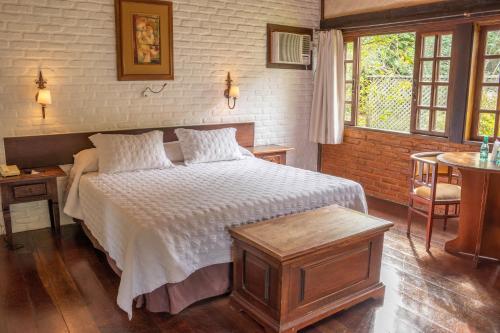 a bedroom with a bed and a table and windows at Bomtempo Itaipava by Castelo Itaipava in Itaipava