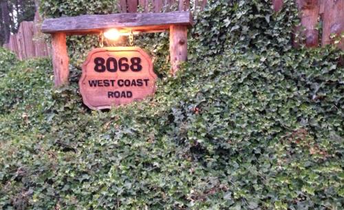 a sign that reads west coast road on a ivy covered fence at Handsome Dan's at Otter Point in Sooke