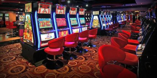 a row of slot machines in a casino with red chairs at Networld Hotel Spa and Casino in Manila