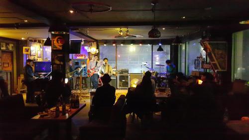 a group of people sitting in a bar with a band on the stage at Gangneung Guesthouse Myu in Gangneung
