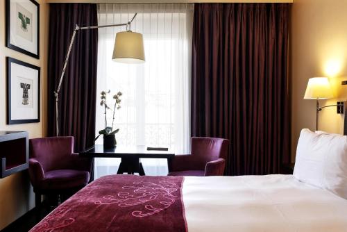 a hotel room with a bed, chair, lamp and window at Eastwest Hôtel in Geneva