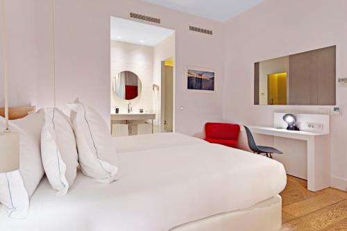 a white bedroom with a large bed and a red chair at One Shot Prado in Madrid