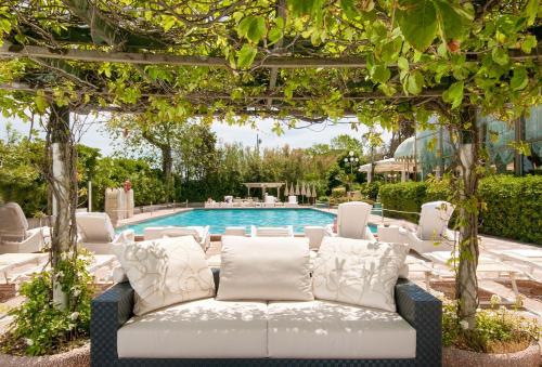 une pergola avec un canapé en face d'une piscine dans l'établissement Grand Hotel Rimini, à Rimini