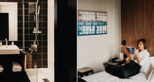 une femme assise sur un lit en train de lire un livre dans l'établissement Best Western Bridge Hotel Lyon East, à Jons