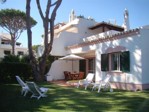 a yard with chairs and an umbrella and a house at SOLAR DO GOLFE - Vilamoura in Vilamoura