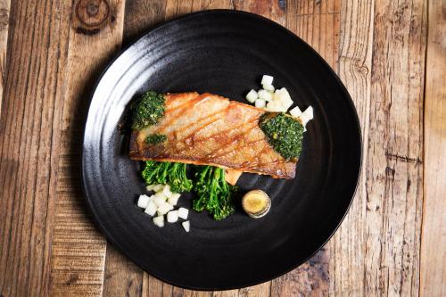 a black plate of fish and broccoli on a wooden table at Fosshotel Nupar in Kálfafell