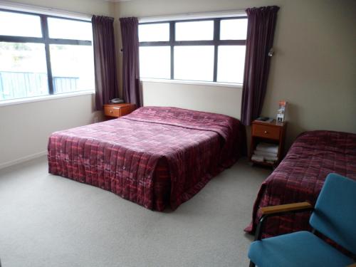 a bedroom with a bed and a chair and two windows at Essex Arms in Huntly