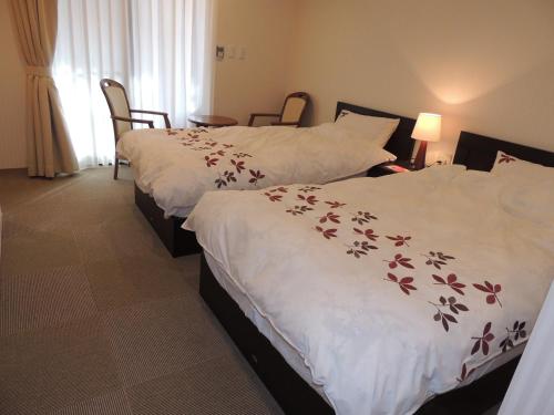 2 camas en una habitación de hotel con sábanas blancas con flores en B&B Hotel Hyochoan en Karuizawa