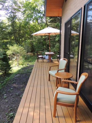a wooden deck with chairs and an umbrella at B&B Hotel Hyochoan in Karuizawa