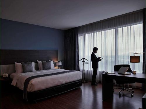 a man standing in a room with a bed and a window at Pullman Kuching in Kuching
