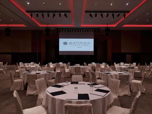 a banquet hall with white tables and chairs and a screen at Pullman Kuching in Kuching
