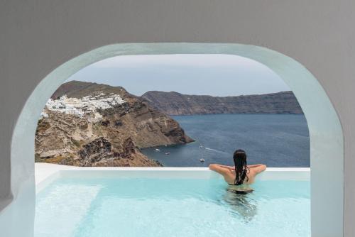a woman sitting in a swimming pool looking out at the ocean at Aspaki by Art Maisons in Oia