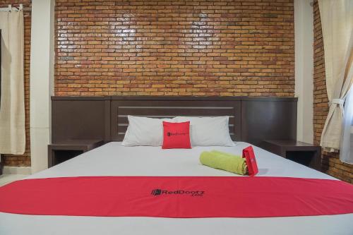 a bed with two red pillows and a brick wall at RedDoorz Plus near Cambridge City Square 2 Medan in Medan