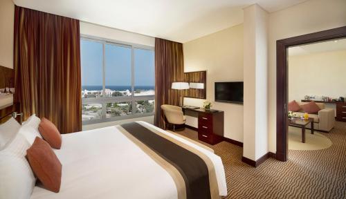 City Seasons Hotel & Suites Muscat في مسقط: غرفة فندقية بسرير ونافذة كبيرة