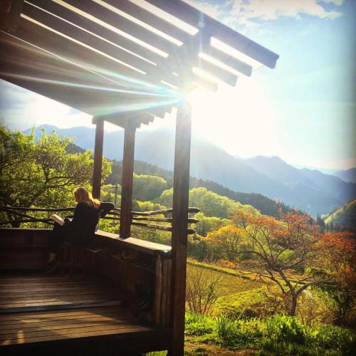 a woman sitting on a porch reading a book at Hostel Yui-an in Nagiso